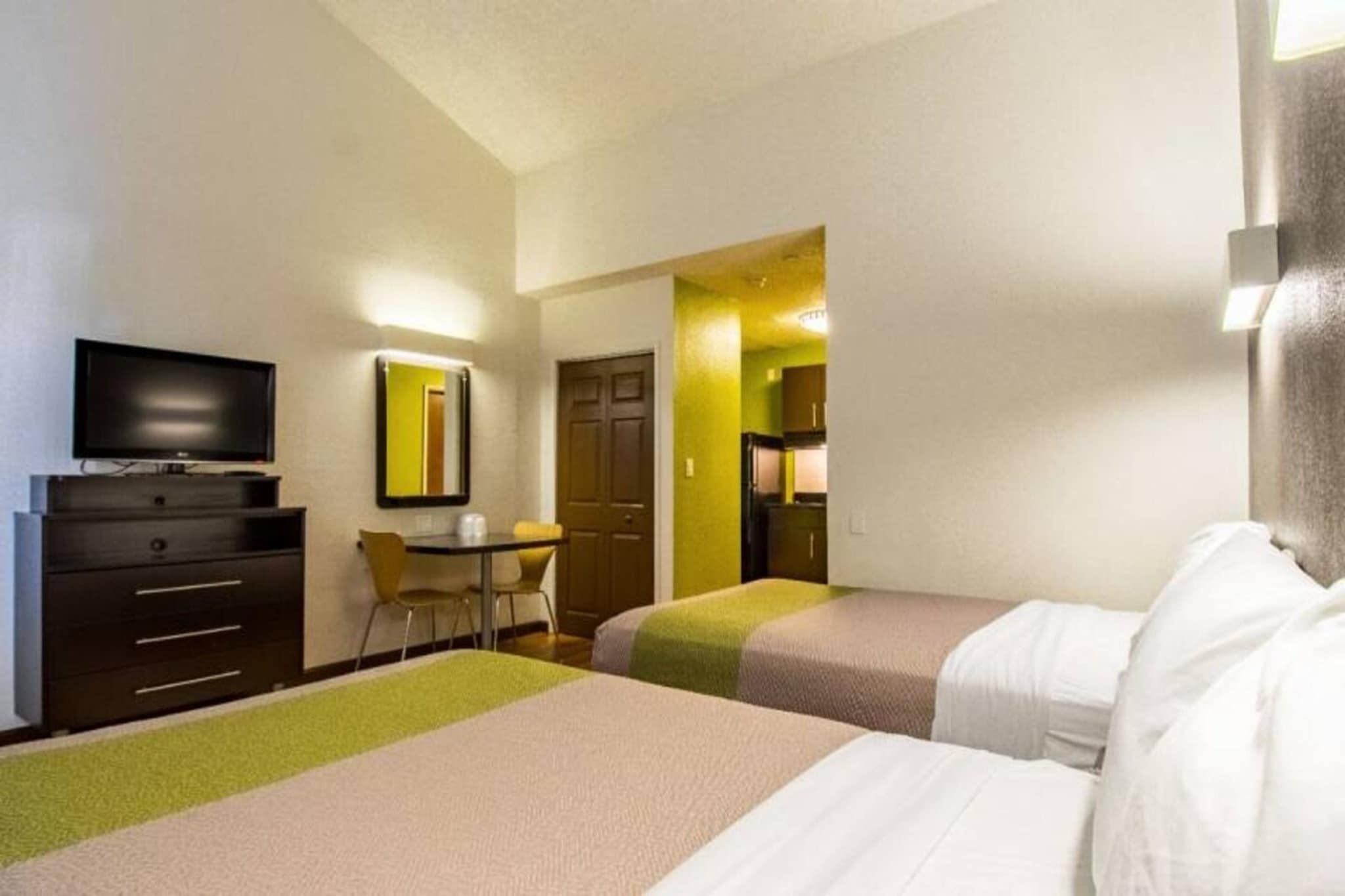 A hotel room with two beds, a desk, a chair, a television, and a mirror.