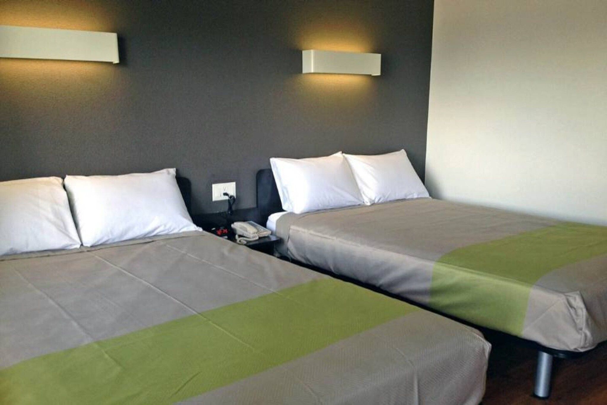 Hotellihuone, jossa on kaksi sänkyä, yöpöytä ja seinälle asennettu puhelin.