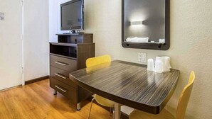 Ett hotellrum med ett träbord, en tv på ett stativ, en spegel på väggen och en stol.