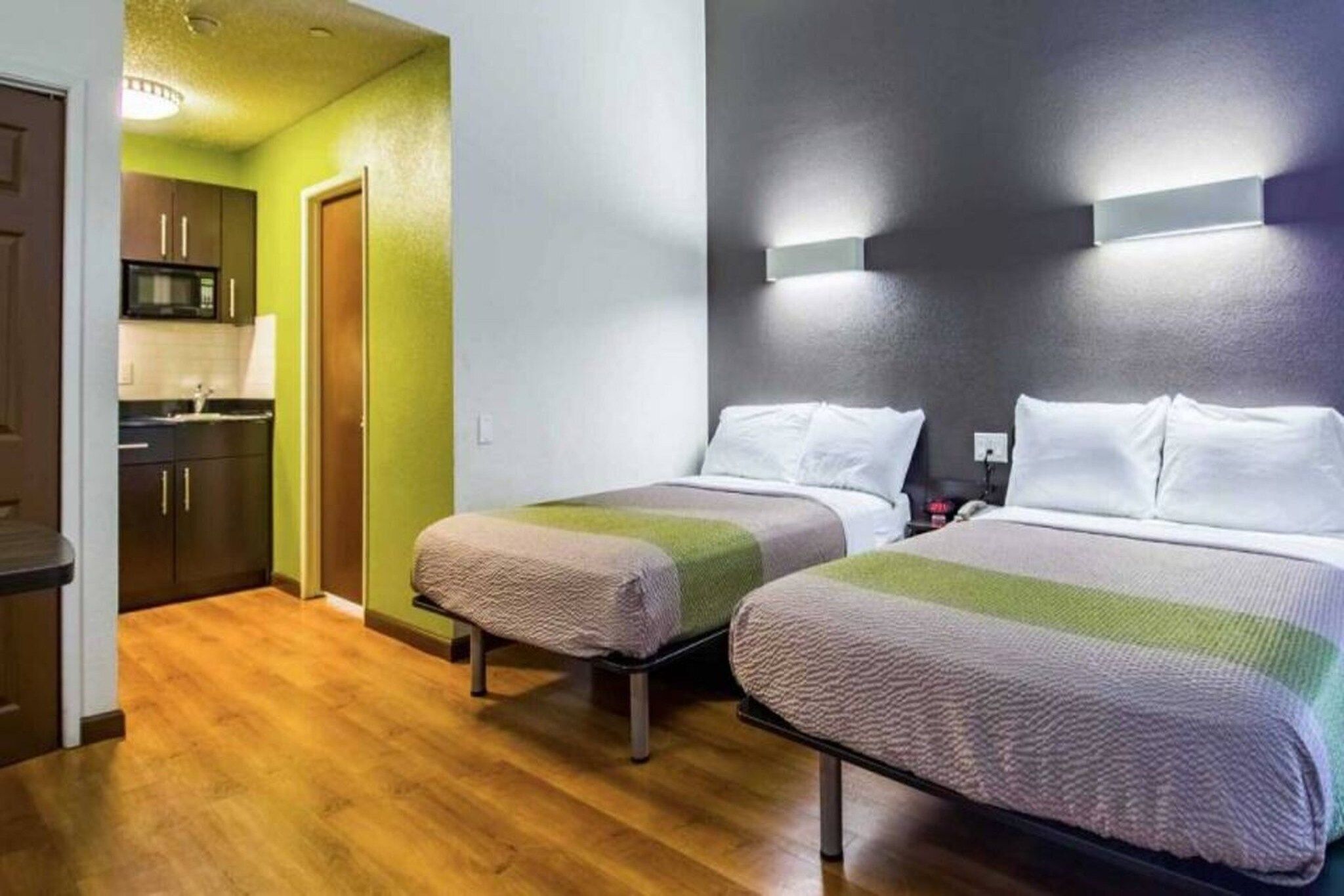 A hotel room with two beds, a kitchenette, and a green wall.