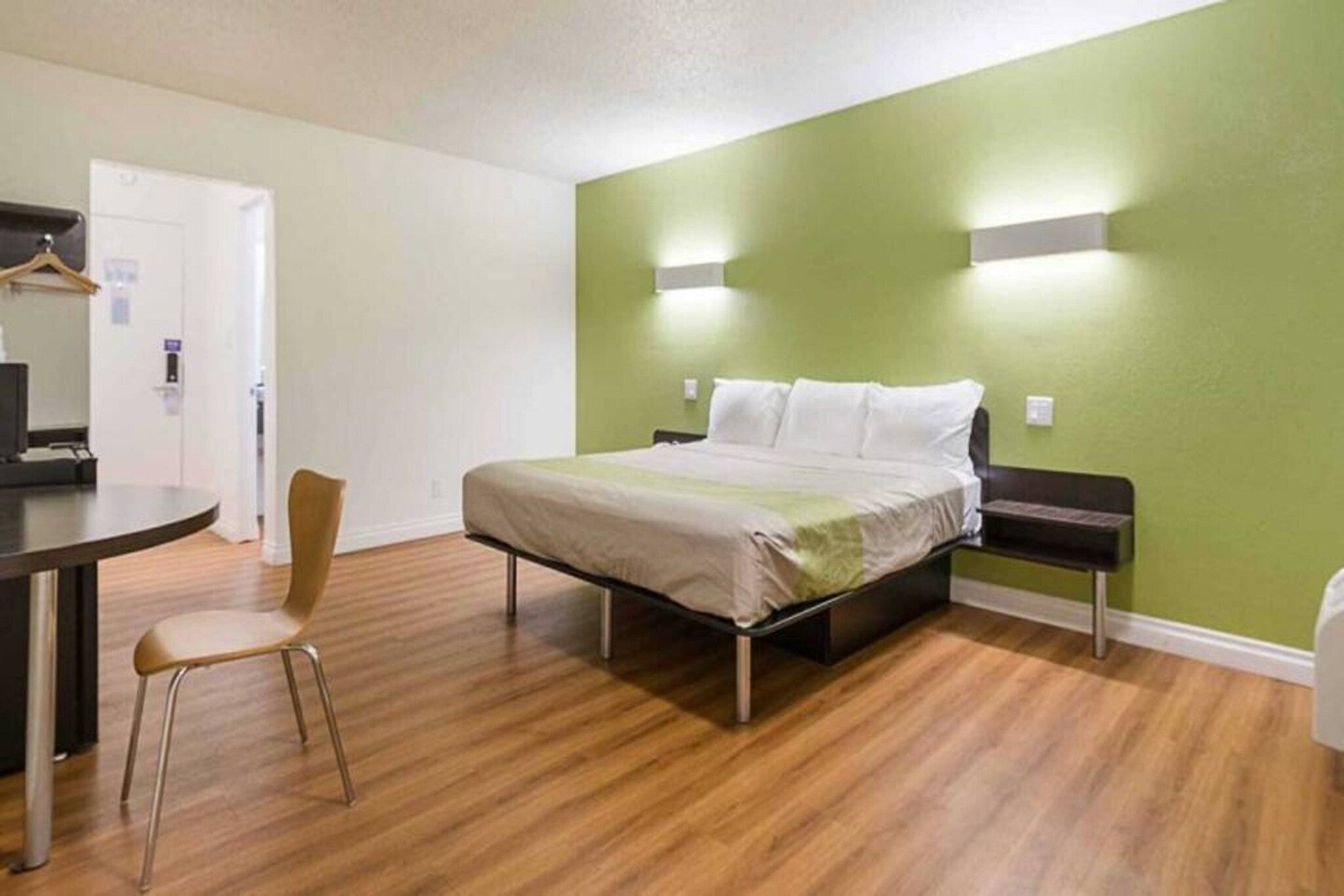 Una cama individual con estructura metálica, una silla, un escritorio e iluminación en la pared.