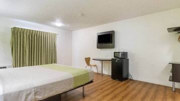Quarto de hotel com cama, escrivaninha, cadeira, televisão e micro-ondas.