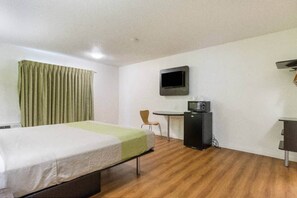 A hotel room with a bed, a desk, a chair, a television, and a microwave.