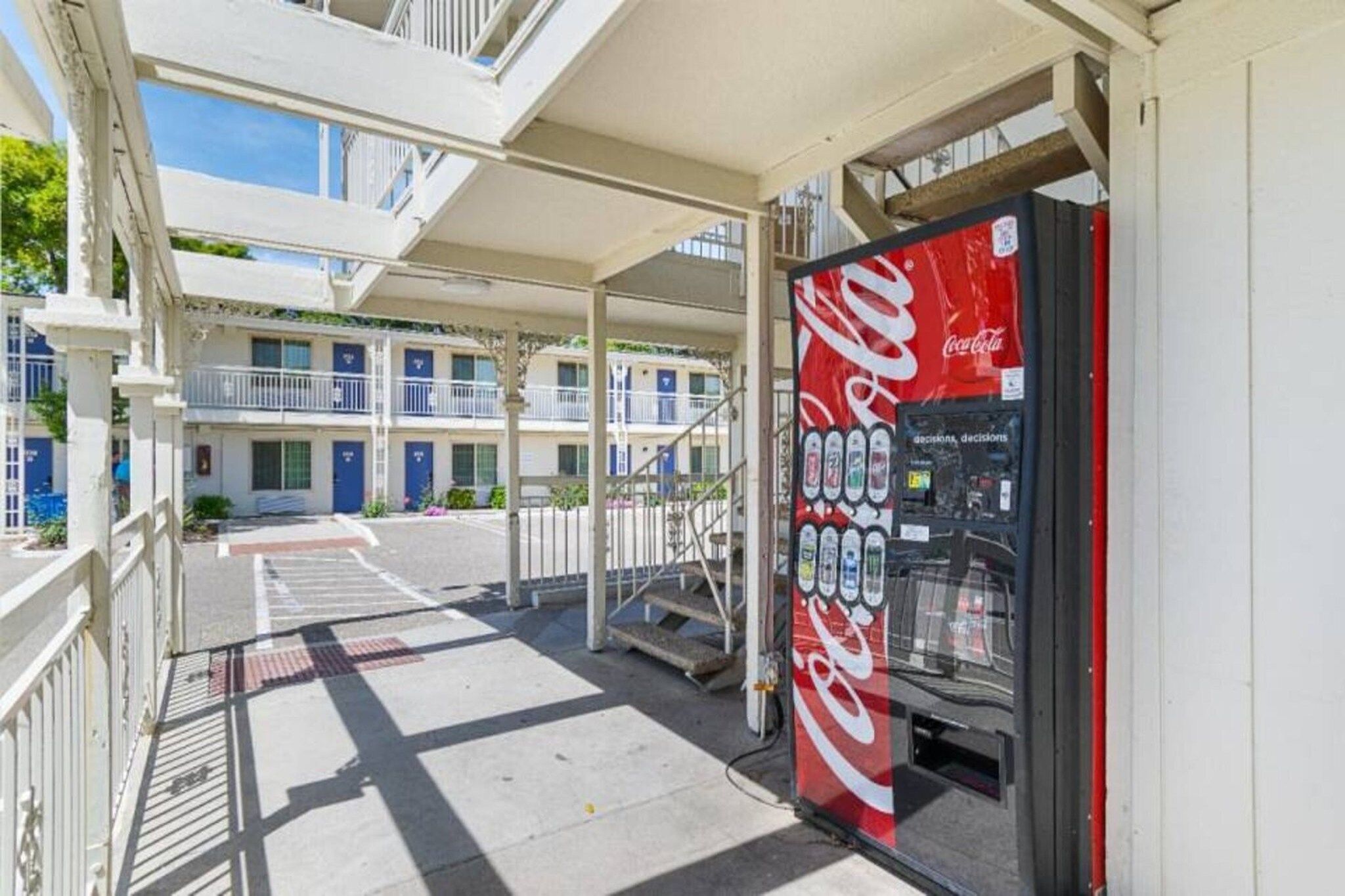 Una máquina expendedora de Coca-Cola en un espacio exterior cubierto, con un edificio al fondo.