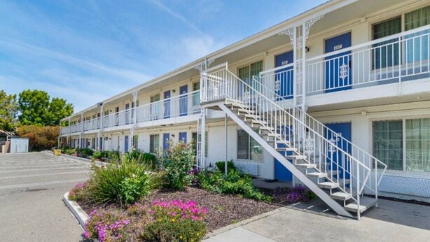Een motel met een centrale trap, meerdere balkons en een aangelegde tuin.