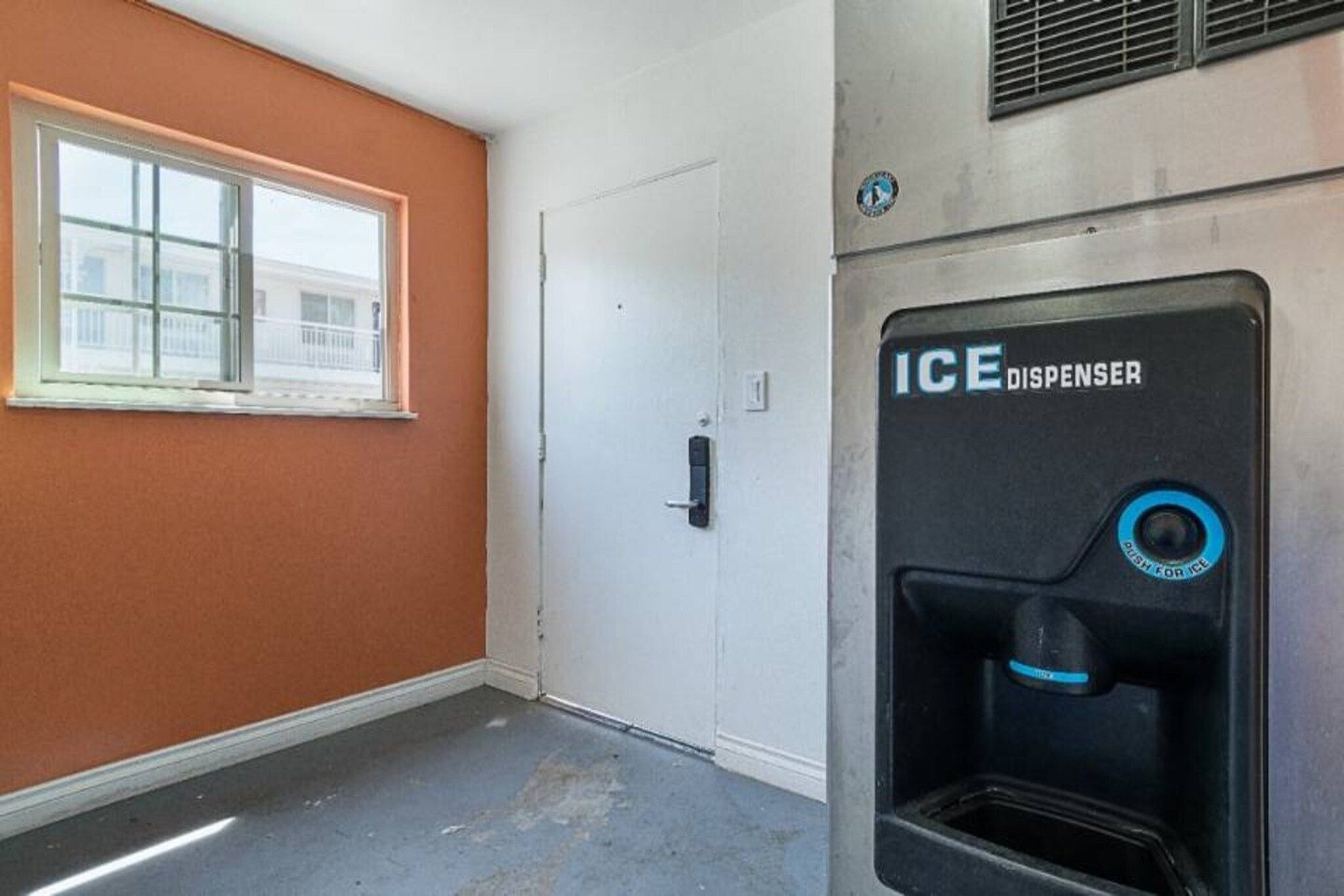 Una habitación con una puerta blanca, un ventanal con vistas y un dispensador de hielo.