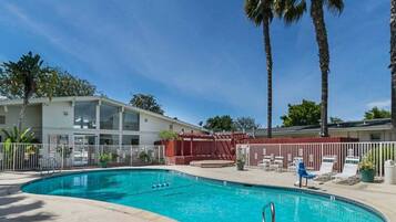 A swimming pool with a fenced area, palm trees, and a building with a white facade.