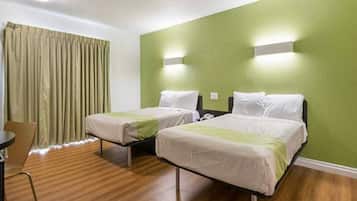 A hotel room with two beds, a wooden floor, a green wall, and a window with curtains.