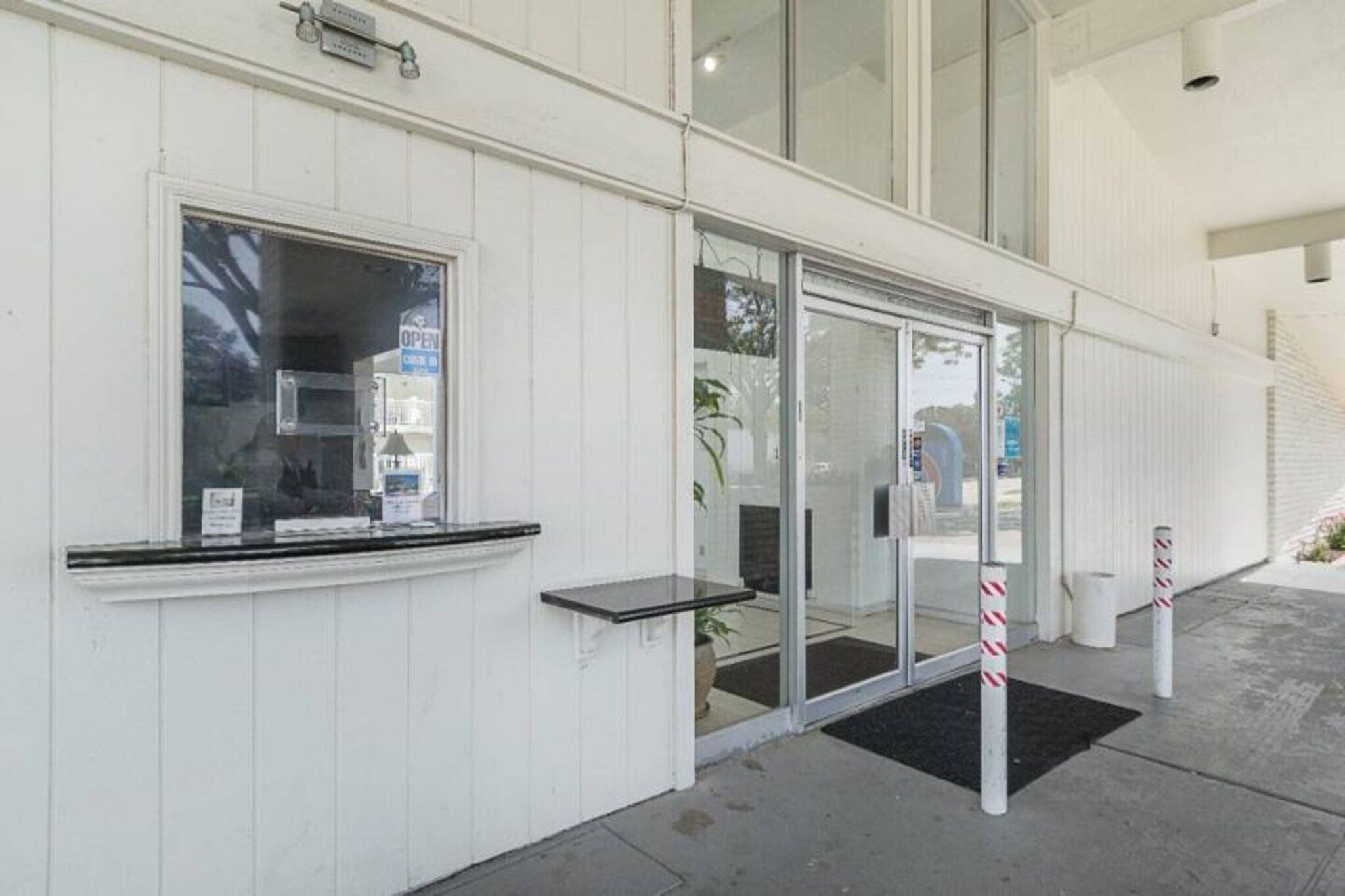A building entrance with a glass door, a small outdoor seating area, and a ramp leading up to the entrance.
