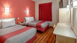 Habitación de hotel con dos camas, un escritorio y televisión.