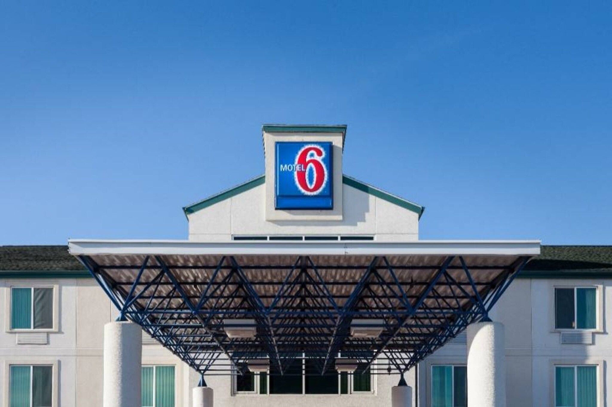 A motel with a prominent '6' sign on the roof, a covered entrance, and a simple facade with windows.