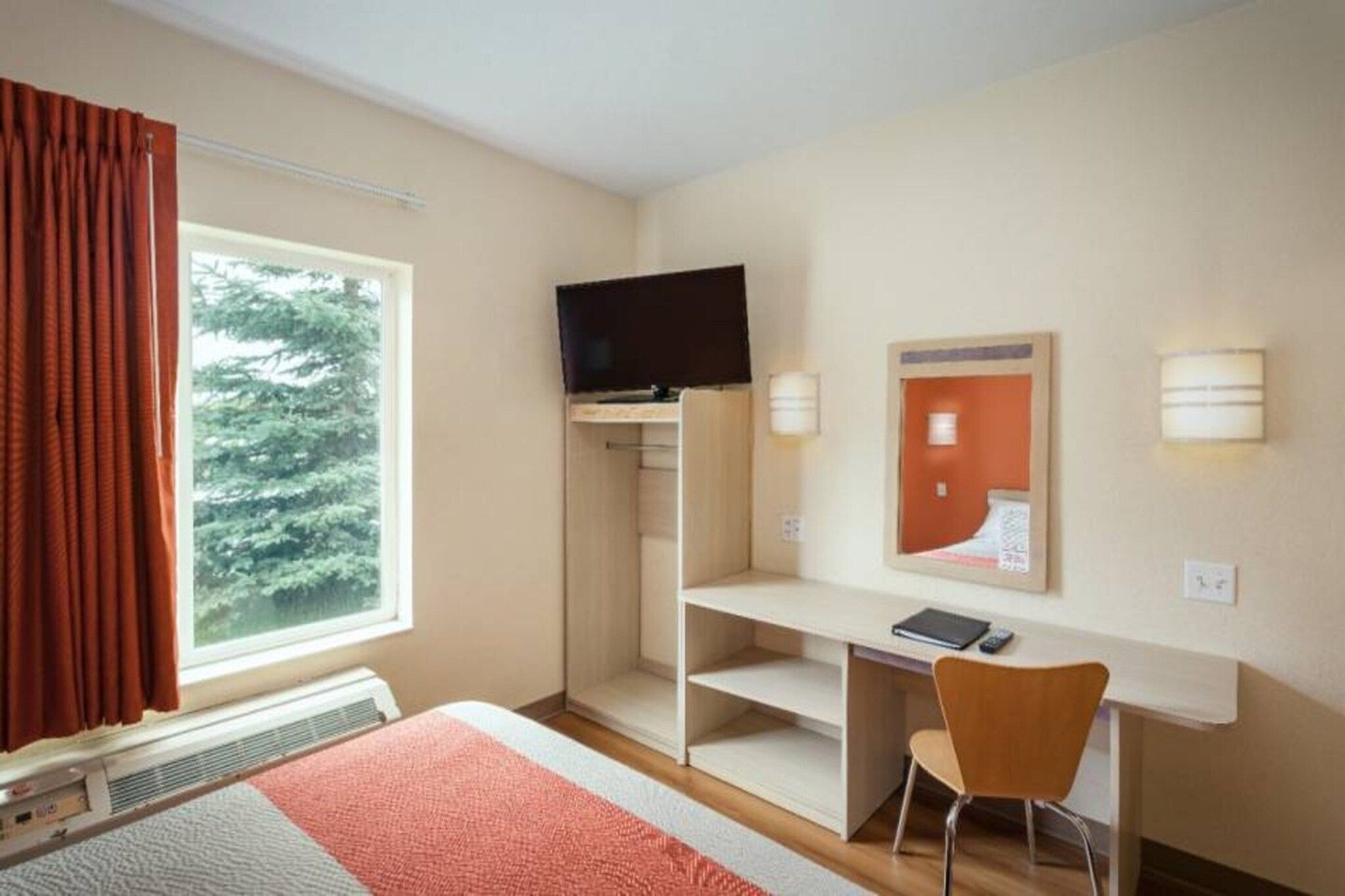 A hotel room with a bed, a desk, a chair, a television, a window, and a mirror.