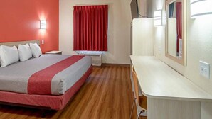 Habitación de hotel con cama, escritorio, espejo y ventana con cortinas rojas.