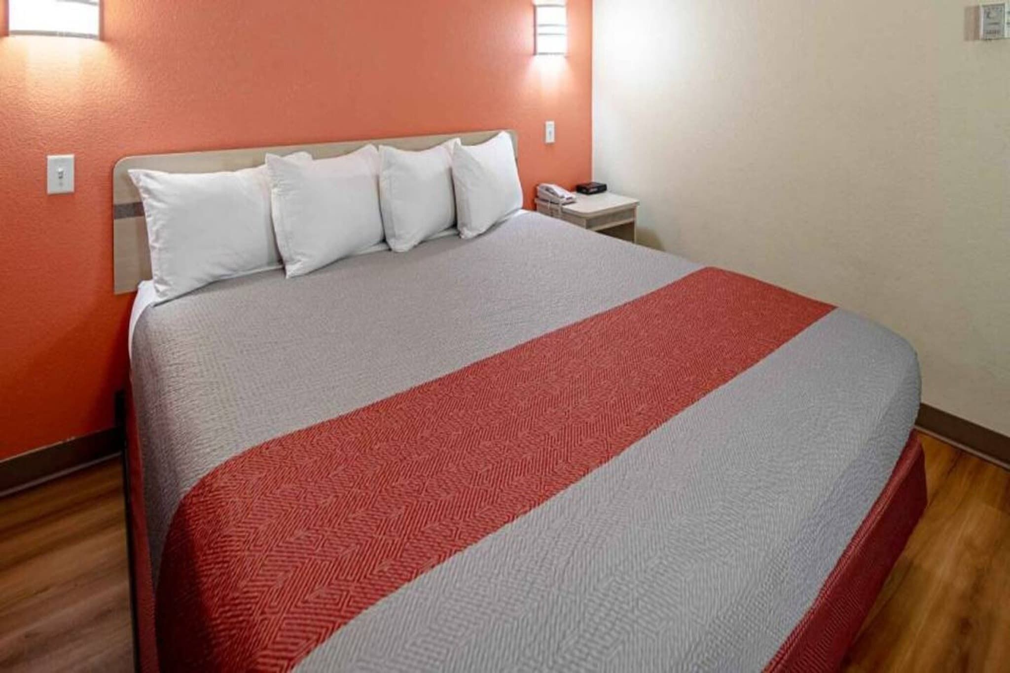 A hotel room with a bed, a nightstand, and a wall-mounted light.