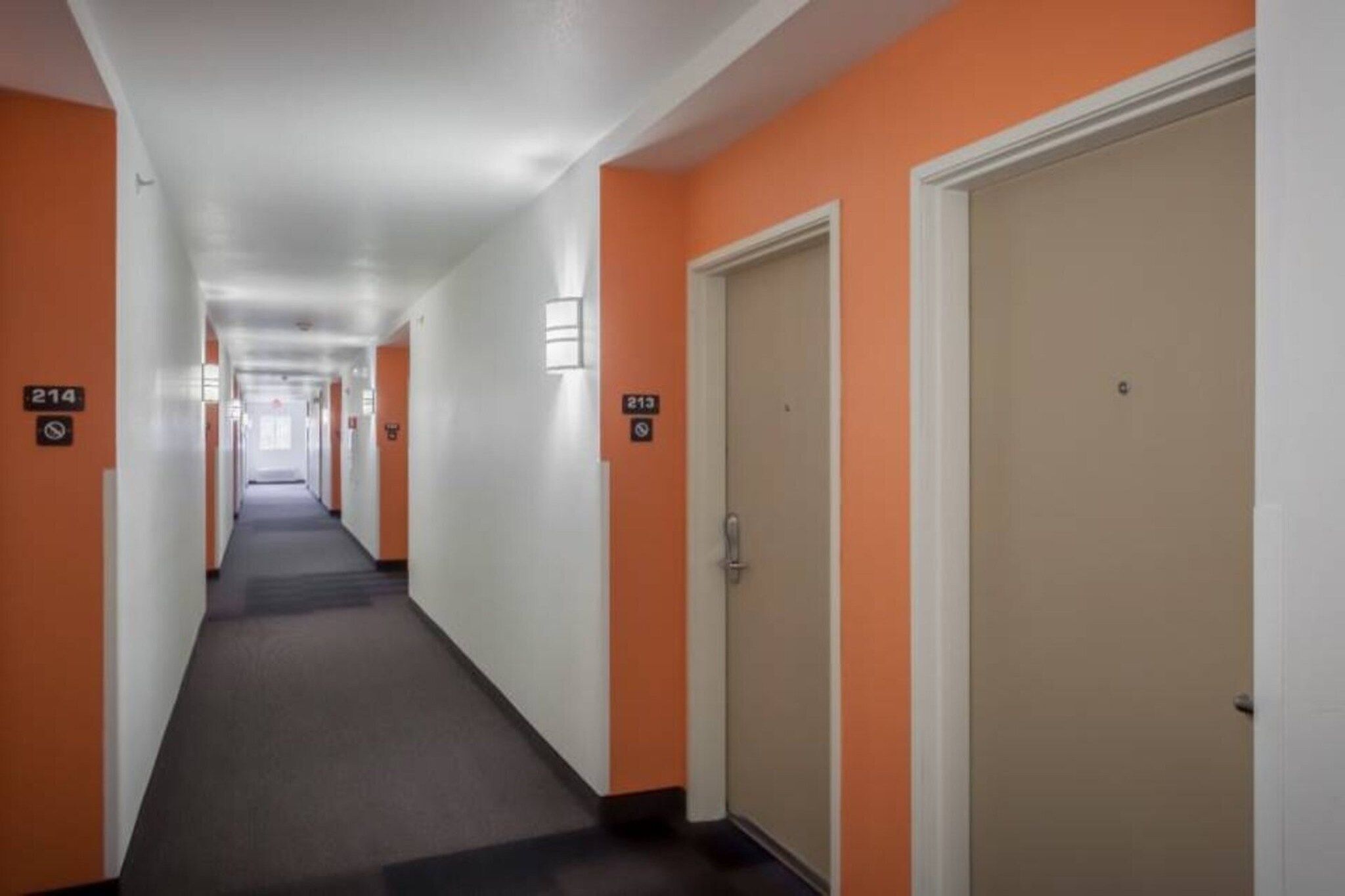 Un pasillo de hotel con puertas numeradas 214 y 213, pisos alfombrados y paredes blancas.