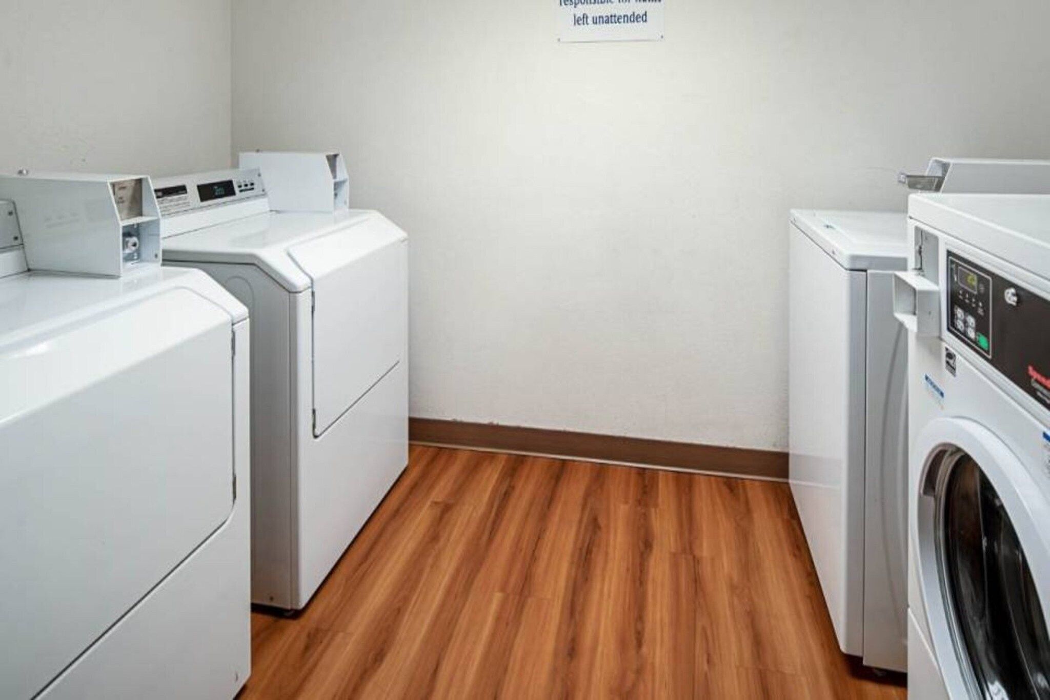 A laundry room with two washing machines and a dryer, wooden flooring, and a sign on the wall.
