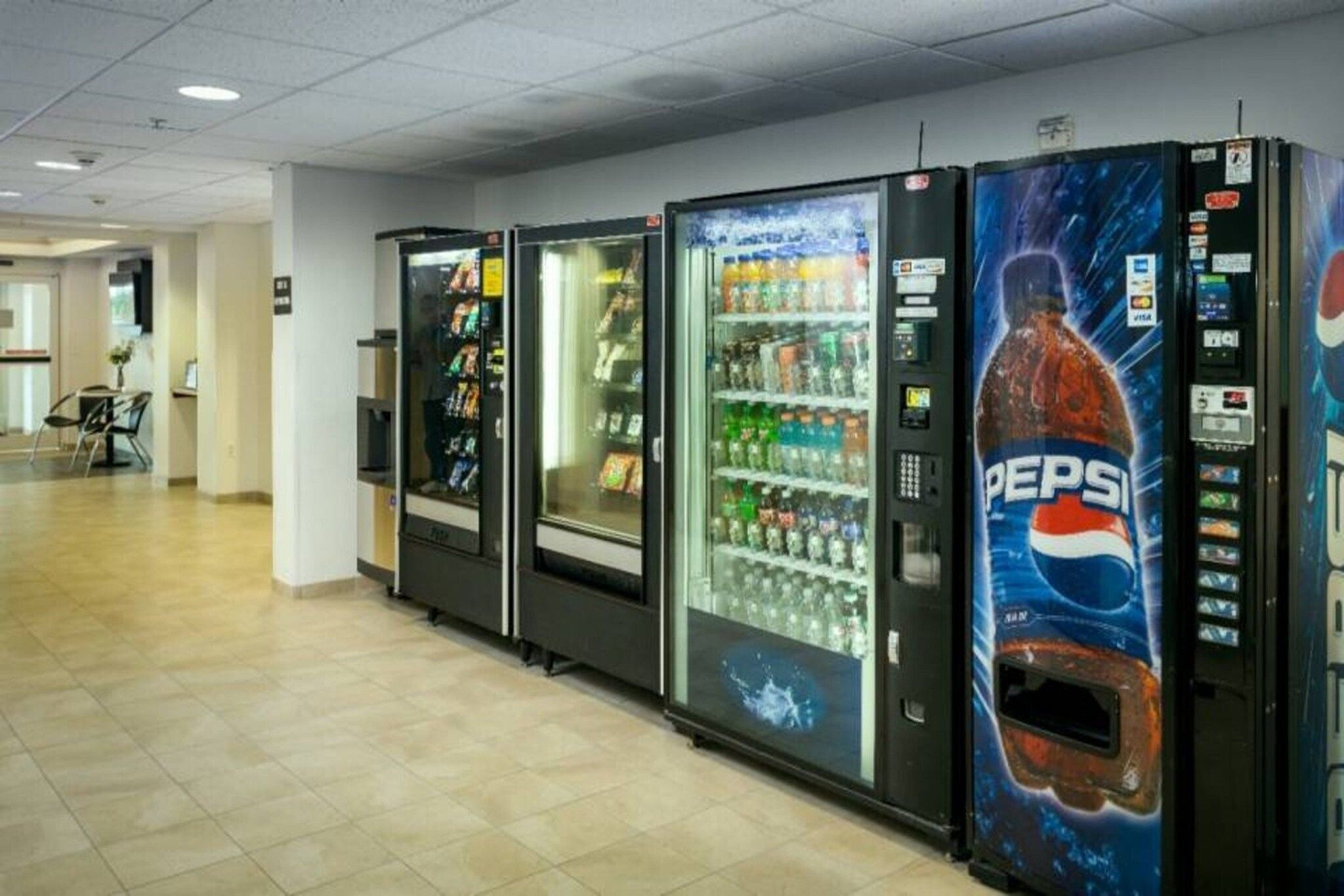 Rivissä on useita automaattikauppakoneita, joissa on Pepsi-logo. Ne sijaitsevat käytävällä, jossa on laattalattia ja taustalla näkyy ovi.