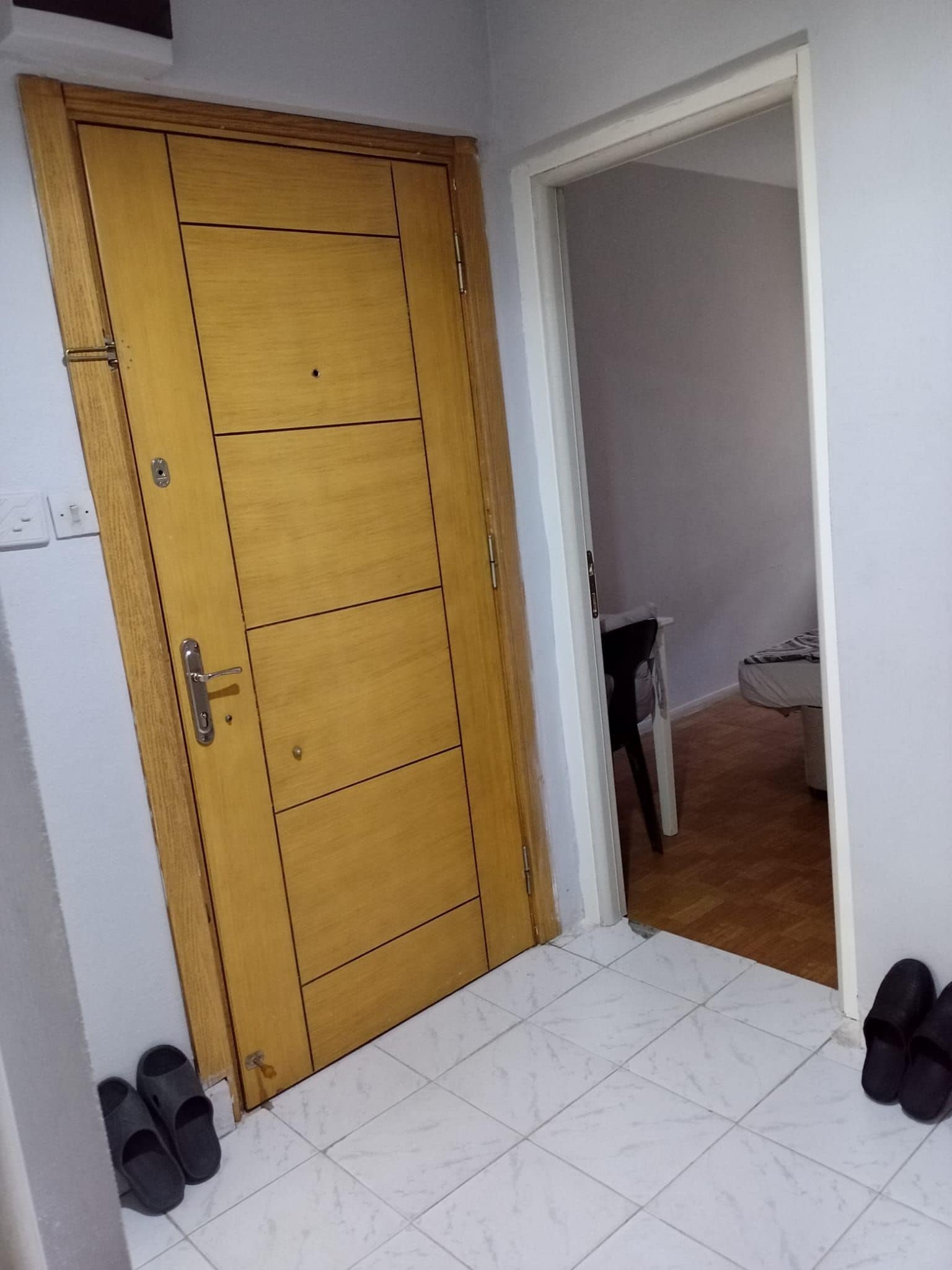 A wooden door with a handle and a keyhole, leading to a room with a bed and a chair.