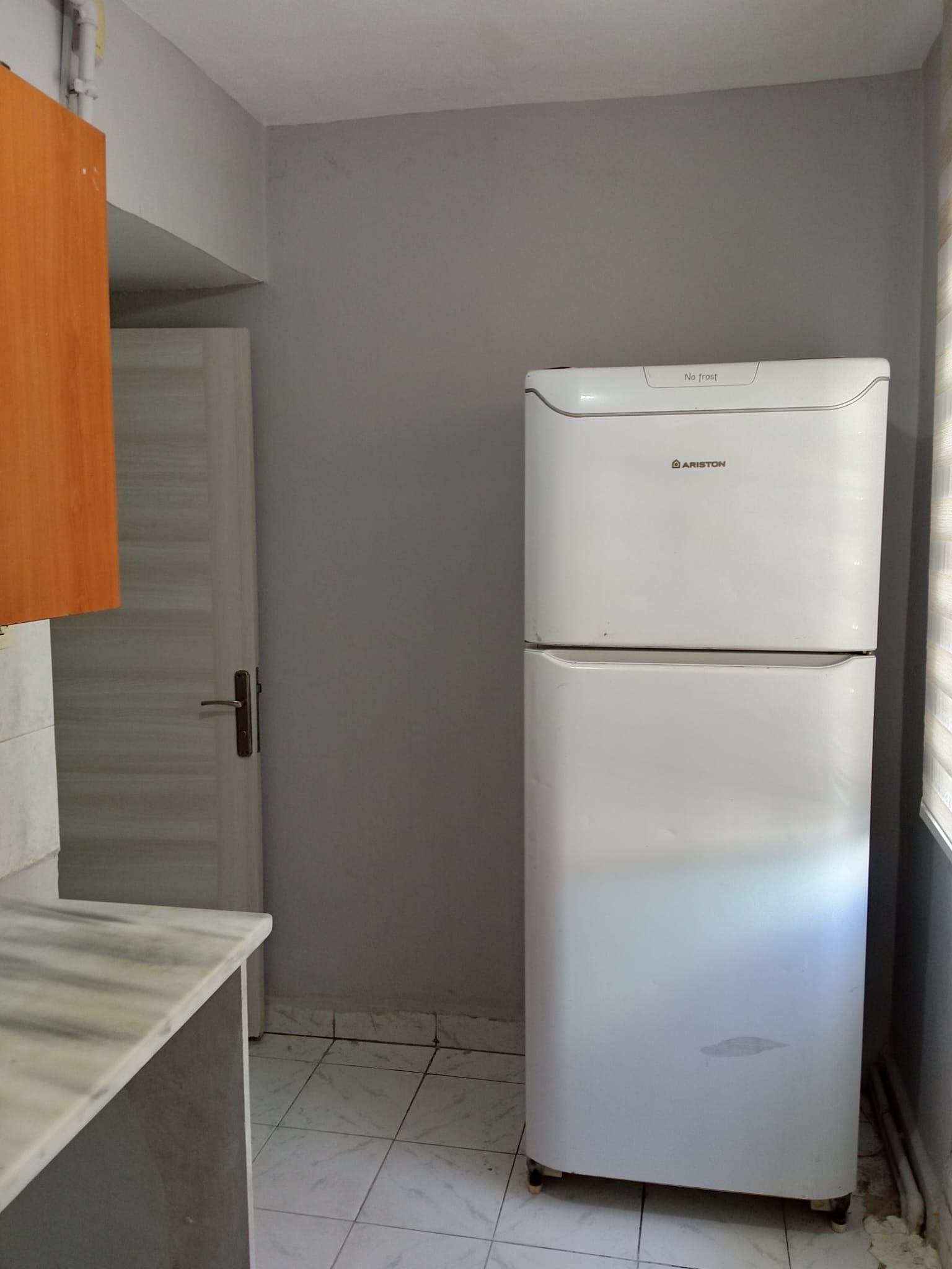 Una cocina compacta con un refrigerador blanco, un armario de madera y piso de baldosas.