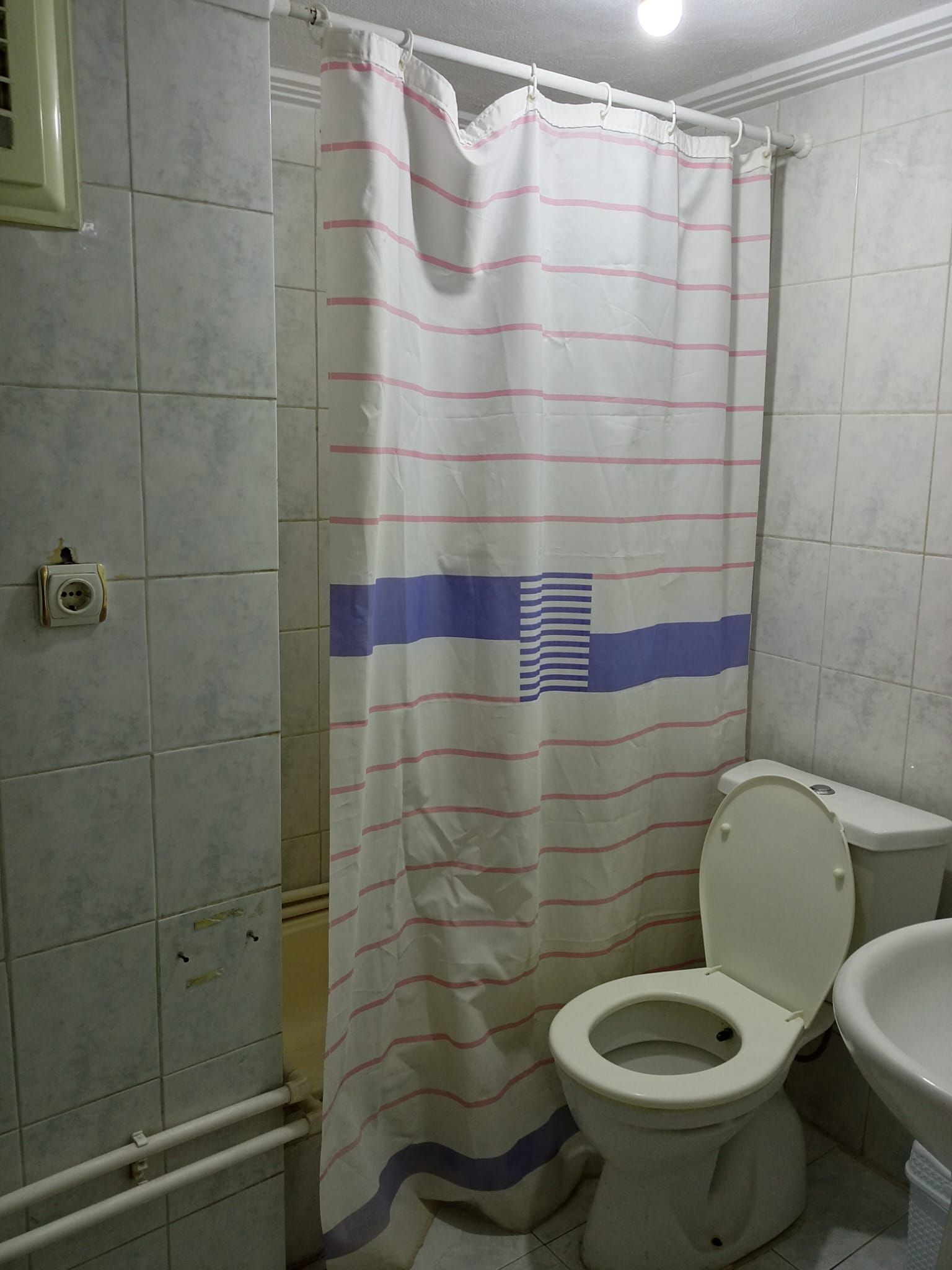 Un baño con inodoro, cortina de ducha con diseño de bandera y paredes de azulejos.