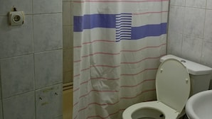 Ein Badezimmer mit Toilette, einer Duschkabine mit Flaggenmuster und gefliesten Wänden.