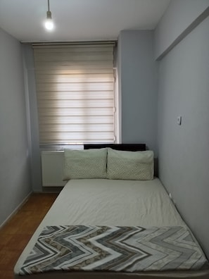 A small bedroom with a single bed, a radiator, and a window with blinds.