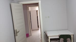 Ein Schlafzimmer mit einem Bett, einem Schreibtisch und einem Stuhl. Eine Tür führt in einen anderen Raum.