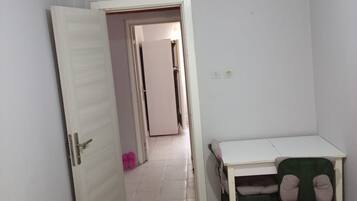 Un dormitorio con cama, escritorio y silla. Hay una puerta que conduce a otra habitación.
