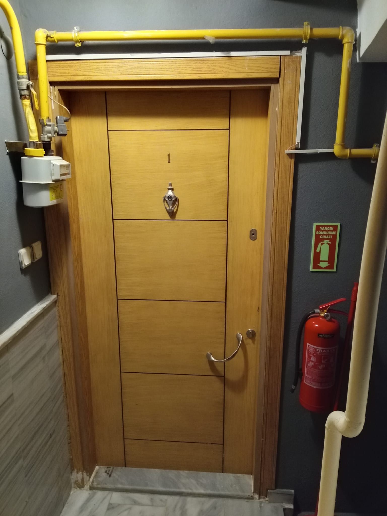 Una puerta de madera con un extintor y un sistema de tuberías amarillo en la parte superior.