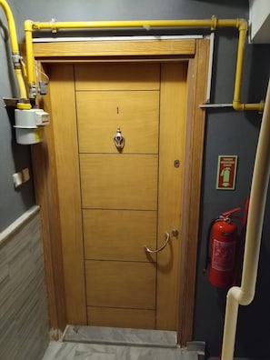 A wooden door with a fire extinguisher and a yellow pipe system above it.
