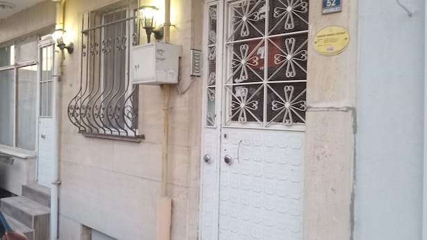 Ein Gebäudeeingang mit einer weißen Tür, Metallgitter vor dem Fenster und einem Schild darüber.