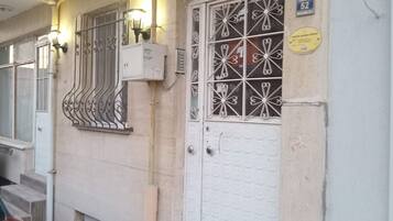 Entrada de un edificio con puerta blanca, rejas metálicas en la ventana y un cartel sobre la puerta.