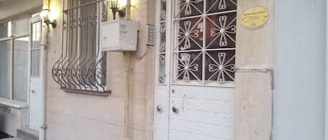 A building entrance with a white door, metal window grills, and a sign above the door.