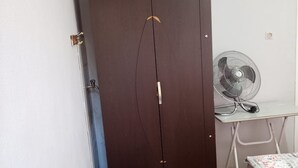 Ein Zimmer mit einem Bett, einem Schreibtisch mit Ventilator, einem Kleiderschrank und einer Heizung.