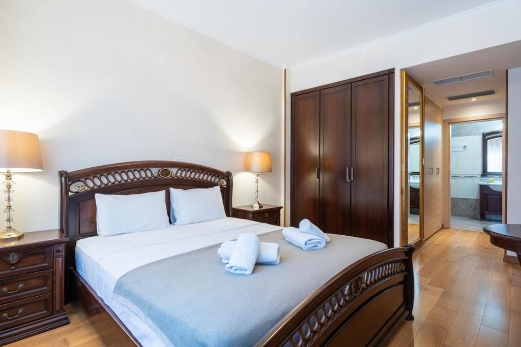 A hotel room with a large bed, wooden wardrobe, and a bathroom visible through an open door.