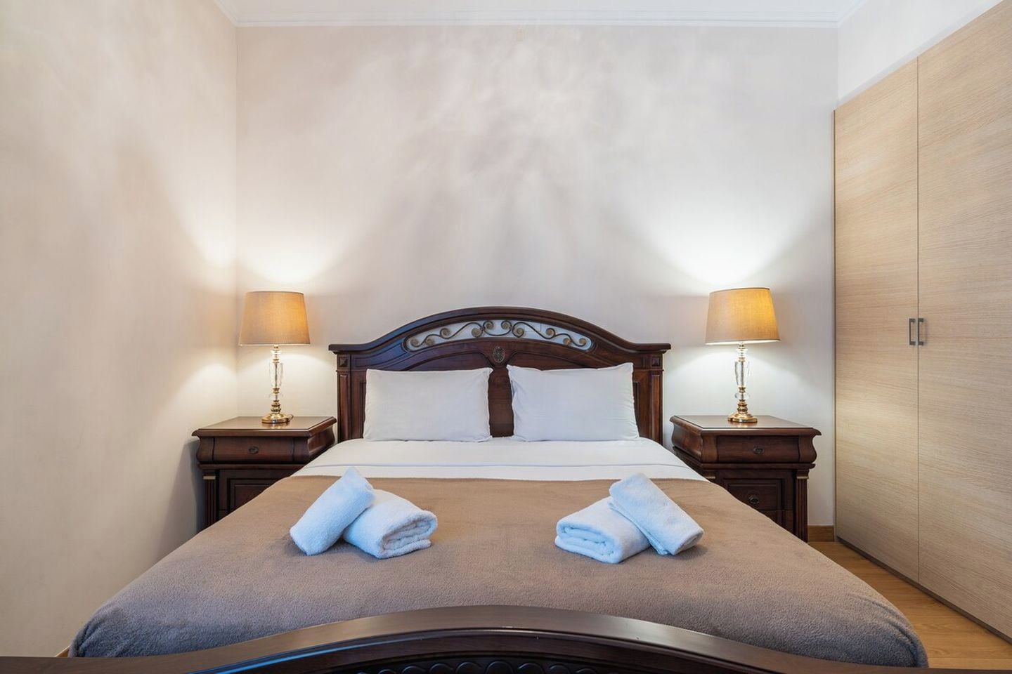 Una habitación de hotel con una cama, dos lámparas de noche, un armario y una toalla doblada sobre la cama.