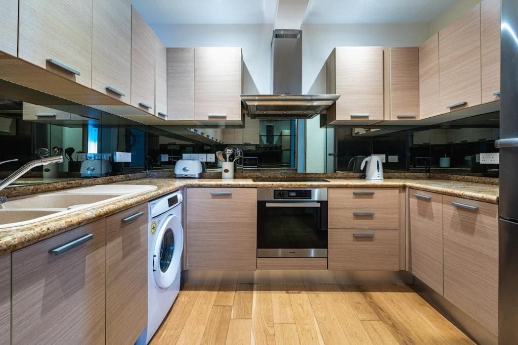 Una cocina moderna con armarios de madera, electrodomésticos de acero inoxidable, lavadora integrada y una isla grande con pileta.