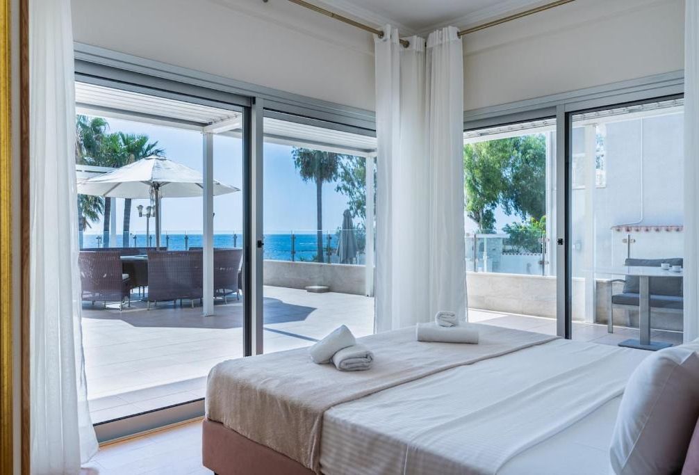 Habitación de hotel con cama, vistas al mar y zona de estar exterior con sombrillas.