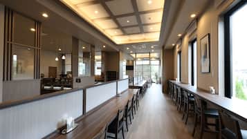 Ein modernes Restaurant-Interieur mit langen Gemeinschaftstischen, hohen Decken mit eingelassener Beleuchtung und großen Fenstern, die viel Tageslicht hereinlassen.