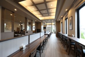 A modern restaurant interior with long communal tables, high ceilings with recessed lighting, and large windows allowing natural light. - HotelRouteInnKobesanda-ShinSandaEkimae- (Sanda)