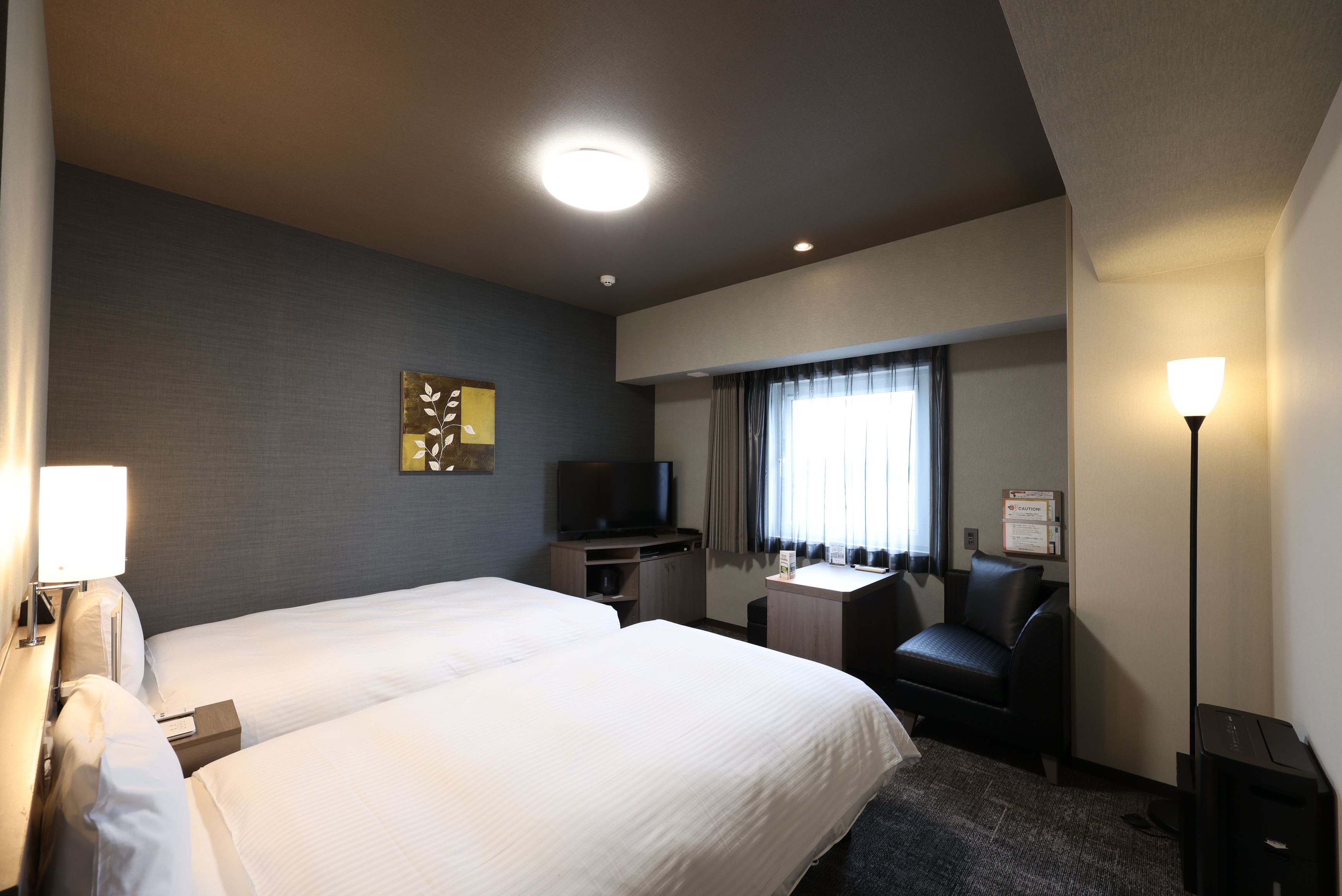 A hotel room with two beds, a desk, a television, a chair, and a lamp.