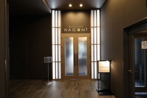 Una entrada moderna con puerta de vidrio, un letrero que indica el nombre 'Restaurant Nagomi' y un cartel de prohibido fumar.