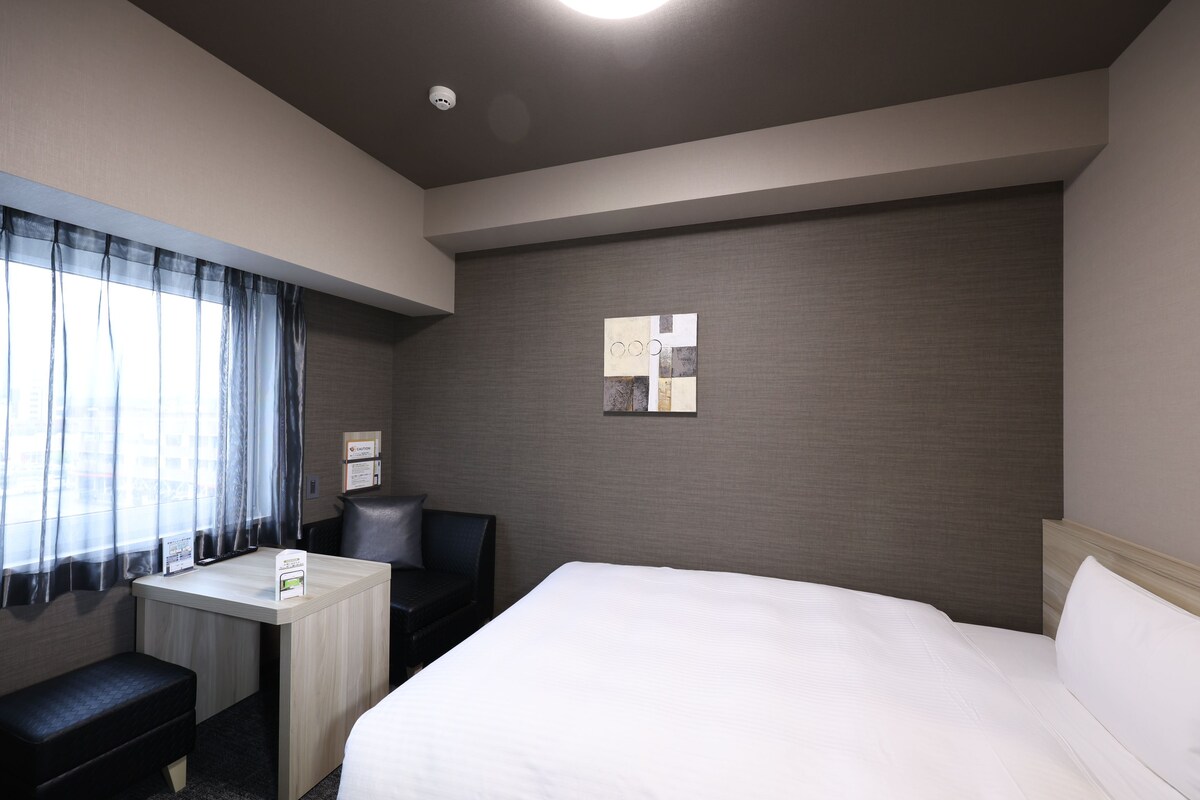 A hotel room with a bed, a desk, a chair, and a small table.