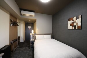 Habitación de hotel con cama, escritorio, silla, unidad de aire acondicionado, un cuadro en la pared y una puerta que da a otra habitación.