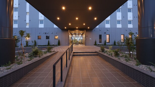 A modern hotel entrance with a covered walkway, tiled flooring, and a clear view of the building's facade. - HotelRouteInnKobesanda-ShinSandaEkimae- (Sanda)