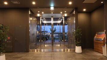 Entrada de hotel con puerta giratoria, detector de incendios y máquina expendedora.