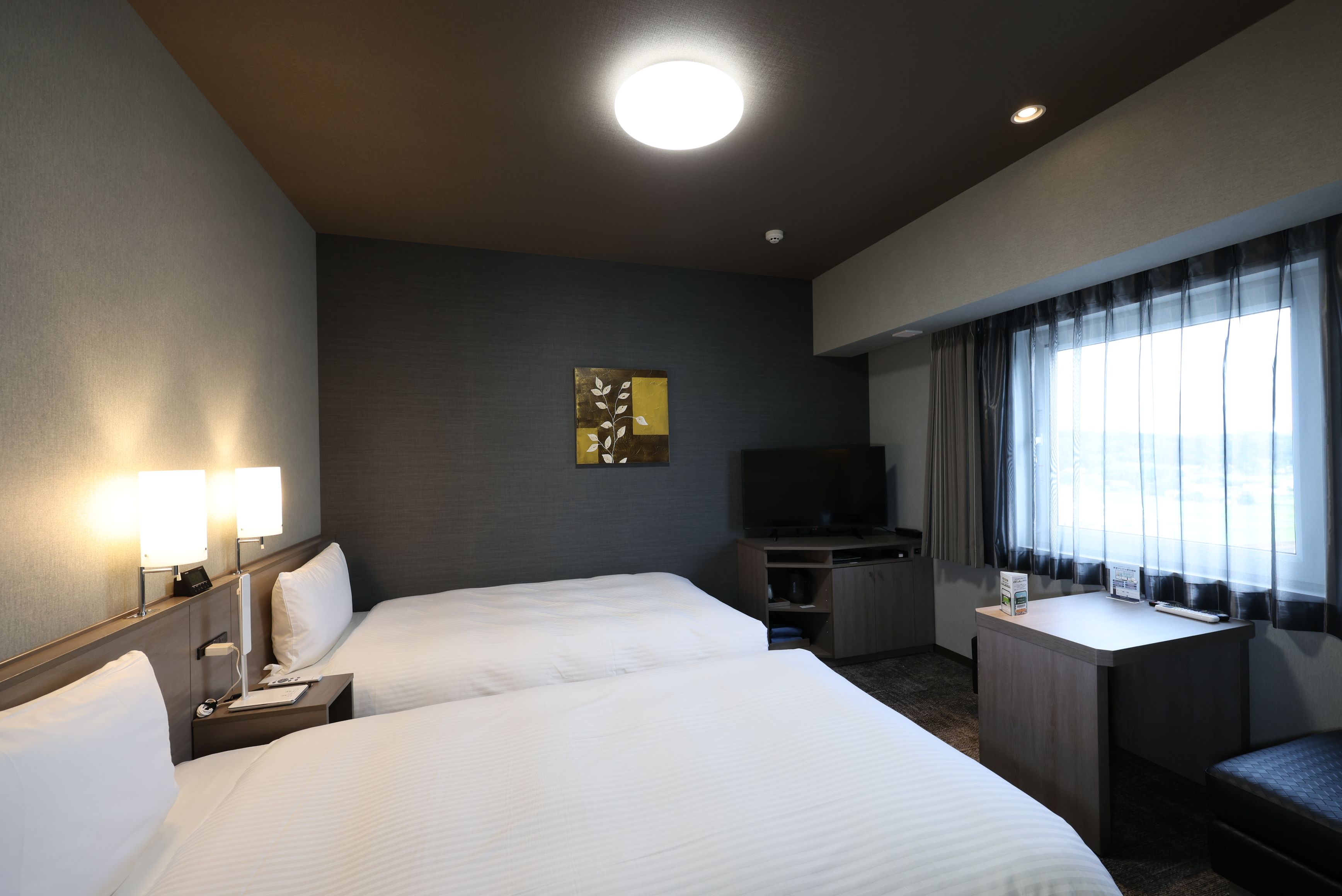 Habitación de hotel con dos camas, un escritorio, un televisor y una ventana con cortinas.