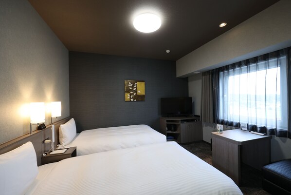 Habitación de hotel con dos camas, un escritorio, un televisor y una ventana con cortinas.