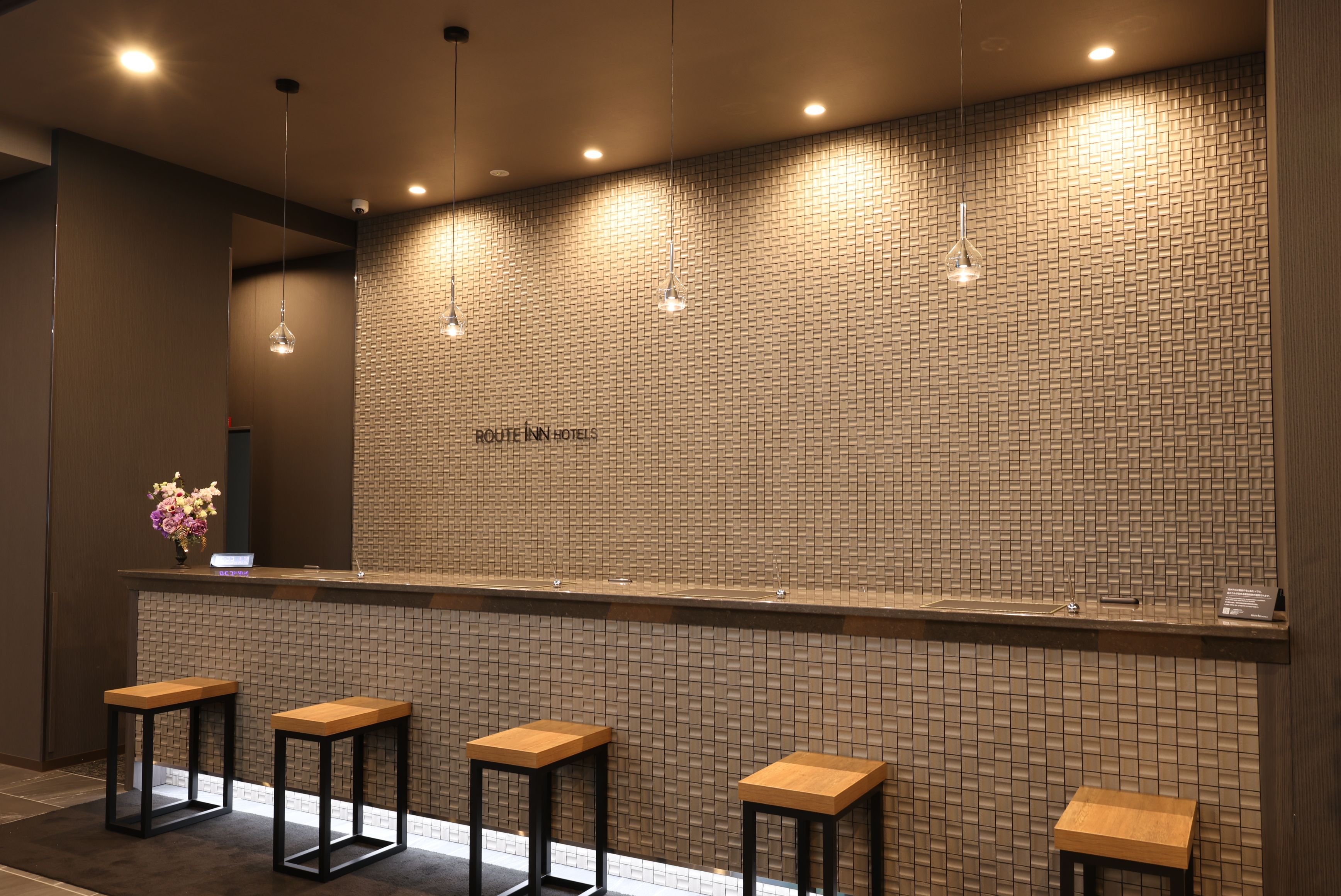 A reception area with a brick-patterned wall, a reception desk, and four wooden stools.