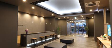 A modern hotel lobby with a reception desk, seating area, and a large skylight.